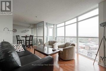 Brampton (Downtown Brampton) condo for rent - A living room with a black couch and a large window overlooking the city.