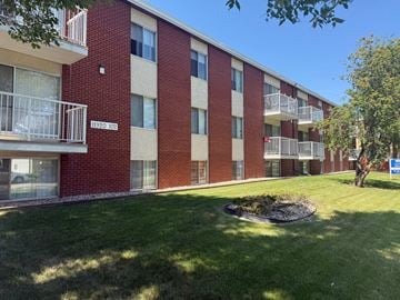 Edmonton apartment for rent - A red brick apartment building with balconies and a green lawn in front.
