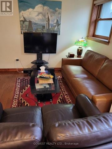 Toronto (High Park North) multi-family for rent - A living room with a brown leather couch and a flat screen TV mounted on the wall.