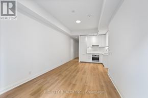 Toronto (Thorncliffe Park) condo for rent - A spacious room with wooden flooring and white walls, featuring a built-in kitchen area with white cabinetry and appliances.