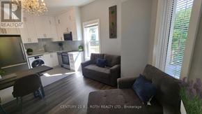 Orillia multi-family for rent - A living room with a couch, chairs, and a kitchen area in the background.