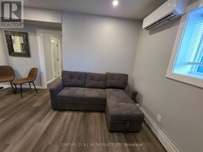 Orillia multi-family for rent - A grey couch in a room with wooden flooring and a window.