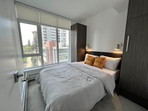 Surrey apartment for rent - A bedroom with a large bed and a view of a building outside the window.