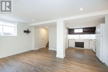Oshawa (Central) apartment for rent - A spacious room with wooden floors and white walls, with a kitchen area visible in the background.