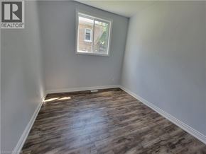 Brantford apartment for rent - A room with wooden flooring and a window showing a building outside.