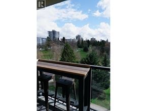 North Vancouver apartment for rent - A balcony with a wooden railing and two stools overlooks a green landscape.
