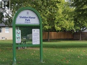 Dundas townhouse for rent - A green sign for Sheldon Manor Park is in front of a fence and trees.