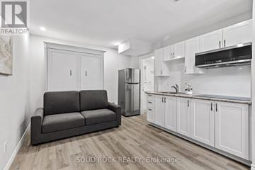 Ottawa fourplex for rent - A living room with a grey couch and a kitchen area with white cabinets.