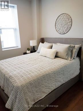 Oshawa (O'neill) multi-family for rent - A bed with a white and grey striped comforter and pillows in a room with a round wall hanging and a small table with a lamp.