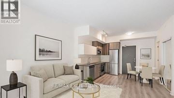 Toronto (Stonegate-Queensway) condo for rent - A well-lit, modern living room with a grey sofa, a dining table set for four, and a kitchen area in the background.