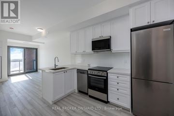 Clarington (Bowmanville) condo for rent - A kitchen with white cabinets and a stainless steel refrigerator.