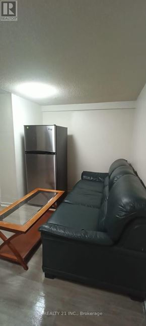 Toronto (Clairlea-Birchmount) apartment for rent - A black leather couch sits in a room with a wooden coffee table and a stainless steel refrigerator.
