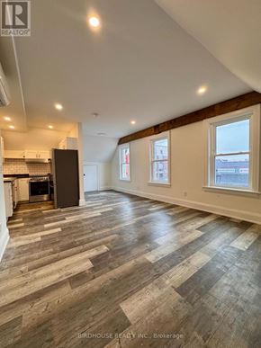 Kawartha Lakes (Lindsay) apartment for rent - A spacious room with wood flooring and a kitchen area with a refrigerator.