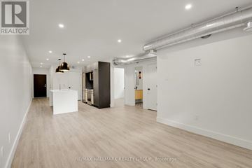 Ottawa multi-family for rent - A spacious room with white walls and wooden flooring, featuring a kitchenette with a sink and a refrigerator.