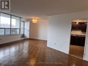 Toronto (Flemingdon Park) condo for rent - A room with wooden flooring and a kitchen area in the background.