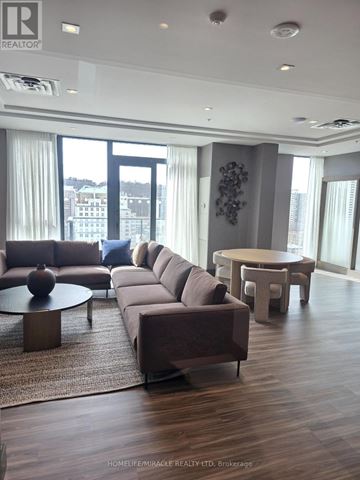 Hamilton (Corktown) condo for rent - A living room with a brown couch and a round table with a vase on it.