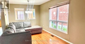 Markham (Berczy) apartment for rent - A living room with a grey couch and a window with a view of a brick building.