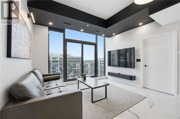 Ottawa condo for rent - A living room with a grey couch and a large window overlooking a cityscape.