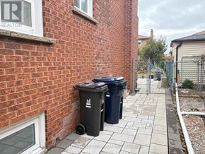 Toronto (Steeles) apartment for rent - A black trash can with a white logo sits on a sidewalk next to a brick wall.