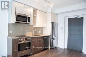 Toronto (Mimico) condo for rent - A kitchen with a stove top oven, microwave, refrigerator, and sink.