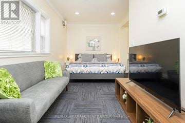 Ottawa apartment for rent - A living room with a grey couch, a bed with a blue and white comforter, and a television on a wooden stand.