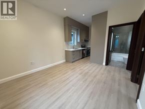 Vancouver apartment for rent - A spacious room with light wood flooring and a kitchen area in the background.