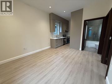 Vancouver apartment for rent - A spacious room with light wood flooring and a kitchen area in the background.