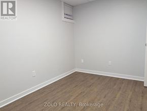 Barrie (Grove East) apartment for rent - A room with wooden flooring and white walls, with a logo that reads "REALTOR" in the top left corner.