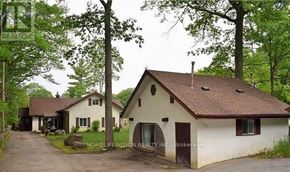 Wasaga Beach apartment for rent - A white house with a brown roof is surrounded by trees.