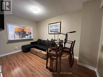 London North (North G) townhouse for rent - A living room with a black couch, a wooden dining table with chairs, and a cardboard box on the floor.