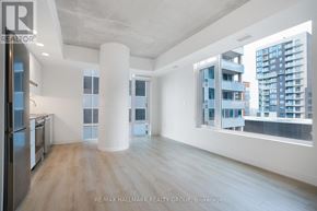 Ottawa condo for rent - A spacious, empty room with a kitchen area and a view of a cityscape through the windows.