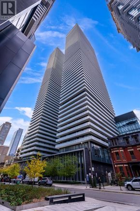 Toronto (Church-Yonge Corridor) condo for rent - A tall building with a unique triangular top is the centerpiece of a city street scene.