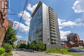 Ottawa condo for rent - A tall building with many windows is surrounded by other buildings and trees.