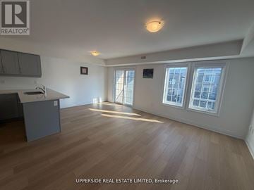 Barrie townhouse for rent - A spacious room with wooden flooring and a kitchen area with a counter and cabinets.