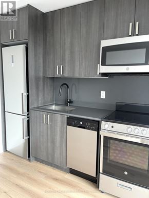 Toronto (Dovercourt-Wallace Emerson-Junction) condo for rent - A modern kitchen with a white fridge, black oven, and a microwave above the stove.