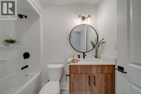 Tecumseh apartment for rent - A bathroom with a white toilet, a round mirror, and a wooden cabinet.