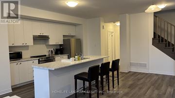 Welland (Dain City) townhouse for rent - A kitchen with white cabinets and a white island with four black chairs.