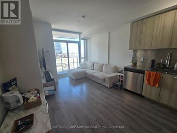 Toronto (York University Heights) condo for rent - A living room with a white couch and a kitchen area with a stainless steel refrigerator.