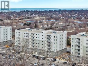 Windsor condo for rent - Apartment buildings with a parking lot in front and a body of water in the distance.