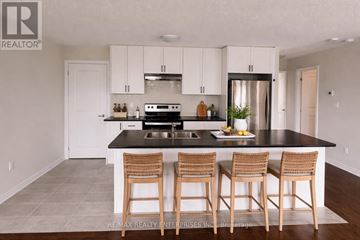 Barrie apartment for rent - A kitchen with white cabinets and a black countertop with a sink and three barstools.