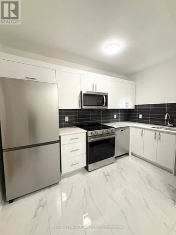 Ottawa apartment for rent - A modern kitchen with a stainless steel refrigerator, microwave, oven, and white cabinets.