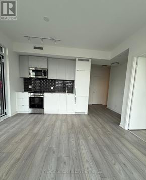 Toronto (South Parkdale) condo for rent - A modern kitchen with white cabinets and a black backsplash.