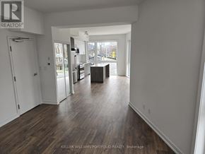 Toronto (Birchcliffe-Cliffside) townhouse for rent - A large empty room with wood flooring and a kitchen area in the background.