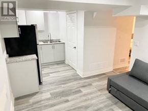 Mississauga (East Credit) apartment for rent - A living room with a grey couch and a kitchen area with white cabinets and a black fridge.