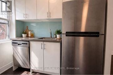 Toronto (Humewood-Cedarvale) multi-family for rent - A stainless steel refrigerator stands in a kitchen with white cabinets and a dishwasher.