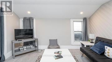 Hamilton (Strathcona) duplex for rent - A living room with a grey couch, a television on a stand, and a window with curtains.