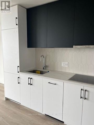 Kitchener condo for rent - A kitchen with white cabinets and a black backsplash.