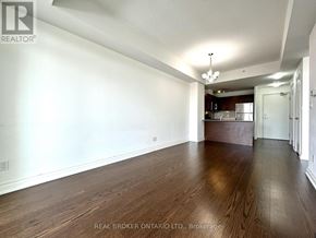 Markham (Old Markham Village) condo for rent - A spacious room with wooden floors and a kitchen area in the background.