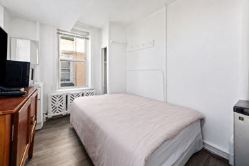 Atlantic City apartment for rent - A bedroom with a bed, a television, and a window with a radiator beneath it.