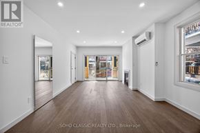 Toronto (The Beaches) duplex for rent - A spacious room with wooden floors and white walls, with a view of a city street through the windows.